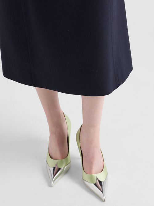 Green high-heeled shoes with metallic tips worn by a person in a black skirt on a light gray background